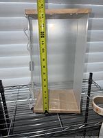 Front view of LED display case showing height measurement with tape measure, clear sides, wooden base and top, and attached LED light cord.