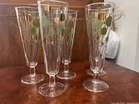 Four clear champagne flutes with green and gold circular design on a wooden surface.