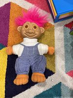Vintage troll doll with pink hair and orange hands and feet lying on a colorful patterned rug.