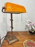 Side view of the orange shade desk lamp on a wooden surface with part of a floral decoration visible.