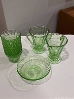 8 green uranium glass dessert cups stacked, double-handled creamer, sugar bowl, and bowl/dish shown on white surface.