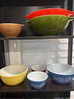 Photo showing 10 vintage Pyrex mixing bowls in assorted colors and designs displayed on shelves.