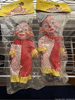 Two vintage clown toys in original sealed packaging with header cards visible, showing their condition and design details.