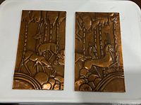 Pair of vintage copper etching panels with embossed nature scenes on a white surface
