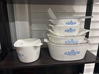 Full view of stacked vintage Corningware blue cornflower pattern dishes on shelf, various sizes and shapes, some with lids.