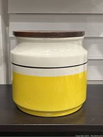 Front and side view of the ceramic cookie jar showing yellow and off-white crock style design with walnut lid.