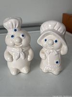 Front view of vintage Pillsbury Doughboy and Doughgal salt and pepper shakers showing details like chef hat, bonnet, and blue painted eyes and buttons.