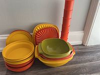Photo of vintage Tupperware including stackable orange containers, yellow and orange plates, green and yellow bowls with handles, and lids.