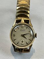 Front view of watch dial showing hour markers, hands, brand name and subsidiary seconds