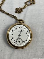 Pocket watch face and attached chain laid on white fabric background