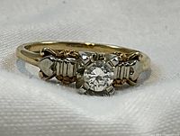 Front view of ring on white fabric, showing diamond and metal detail