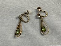 Close-up front view of both earrings on white fabric.