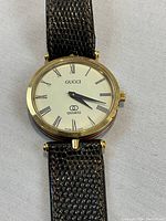 Close-up of watch face showing white dial, Roman numerals, Gucci logo and gold-tone case