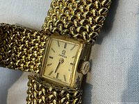 Close-up of rectangular Omega watch face with hidden cover removed, showing gold-tone dial and baton markers