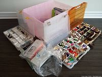 Full view of all items in the lot showing large plastic storage container, multiple compartment boxes full of multicolored Bunka embroidery threads, some smaller boxed accessories and bags.