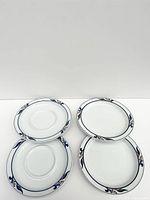 Two white porcelain saucers and two side plates with blue and pink floral border pattern, shown on white background.