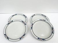 Four white ceramic side plates with blue and orange floral borders arranged on a white surface.