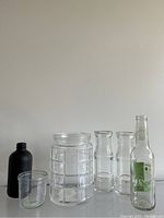 Overview of six vintage glass bottles and jars arranged in a row against a plain background, showcasing varying designs and sizes.