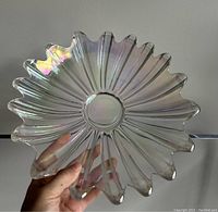 Hand held clear iridescent glass dish showing detailed petal-like scalloped edges and iridescence.