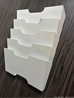Front and angled side views of white metal wall filing unit showing four vertical compartments