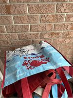Multiple reusable shopping bags stacked together, including a blue Roots branded bag with red handles.