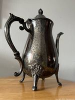 Side view of vintage silverplate teapot showing ornate handle and decorative feet