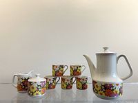 Front view of the 1960s Japanese floral tea set including the teapot, four cups, sugar bowl, and creamer arranged on a clear surface.