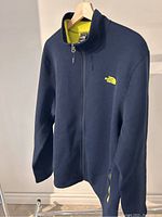 Front view of navy blue The North Face fleece jacket showing yellow logo, zipper, and interior collar lining