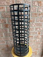 Full view of the tall cylindrical metal basket with a grid pattern for holding umbrellas or bags.