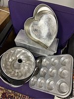 Photo of various vintage bakeware stacked on chair including heart pans, bundt pans, and muffin tin.