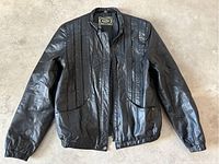 Full view of vintage black leather jacket laid flat, showing pleat and pocket details.