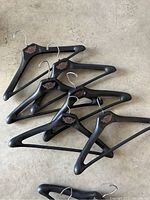 Six black wooden coat hangers with metal hooks laid on floor, visible Harley Davidson emblems on each.