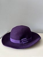 Full view of purple vintage hat showing rounded crown and wide brim with ribbon band and bow.