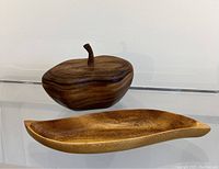 Photo showing the lidded wooden bowl shaped like fruit and the wavy catch all tray on a white surface.