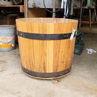 Side view of the large wooden barrel showing its cylindrical shape, wooden slats, and two black metal bands.