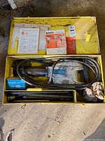 Yellow metal carrying case open showing demolition hammer, cord and bits