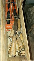 Multiple woodworking chisels with wooden handles and steel blades in wooden box; worn handles and blades