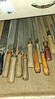 Multiple metal hand files with wooden handles and one with black handle laid out in a drawer, showing condition and variety of tools.