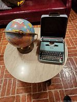 Photo of the globe and the portable typewriter side-by-side on a round table.