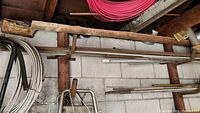 Overall view of copper pipes, metal hoses, and rods stored on wall rack in garage with concrete block wall background.