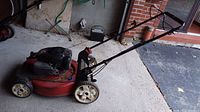 Side view of red Toro push lawn mower showing wheels, engine top, and handlebar.