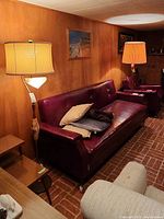 Living room setting showing two Mid-Century Modern floor lamps beside a maroon sofa and wood-paneled wall.