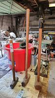 Three sledge hammers standing upright showing wooden handles and metal heads with work area background.