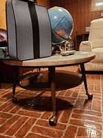 Side and angled view of the round marble top coffee table showing its wooden frame, legs, brass wheels, and lower circular wooden shelf, with some surrounding furniture.