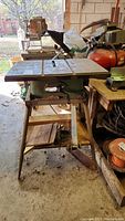 Front side view of table saw showing flat metal top, blade slot, and metal stand with rust.