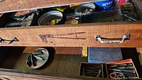 Top drawer of wooden toolbox showing assorted small tools, bits, staples, and miscellaneous hardware.