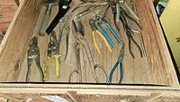 Overview of assorted hand tools including pliers and wrenches inside a wooden drawer.