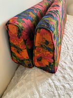 Close-up photo of two wedge bolster cushions showing vibrant floral fabric pattern and piping detail.