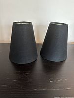 Two black fabric lamp shades shown upright on a flat surface, conical shape with visible minor wear.