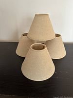 Four beige fabric lampshades group stacked in pyramid shape on black table, showing overall size and color.